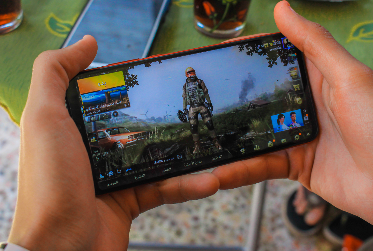 Tangan memegang smartphone menampilkan game mobile bergenre aksi, ilustrasi visual untuk tips game mobile agar jadi pro player.